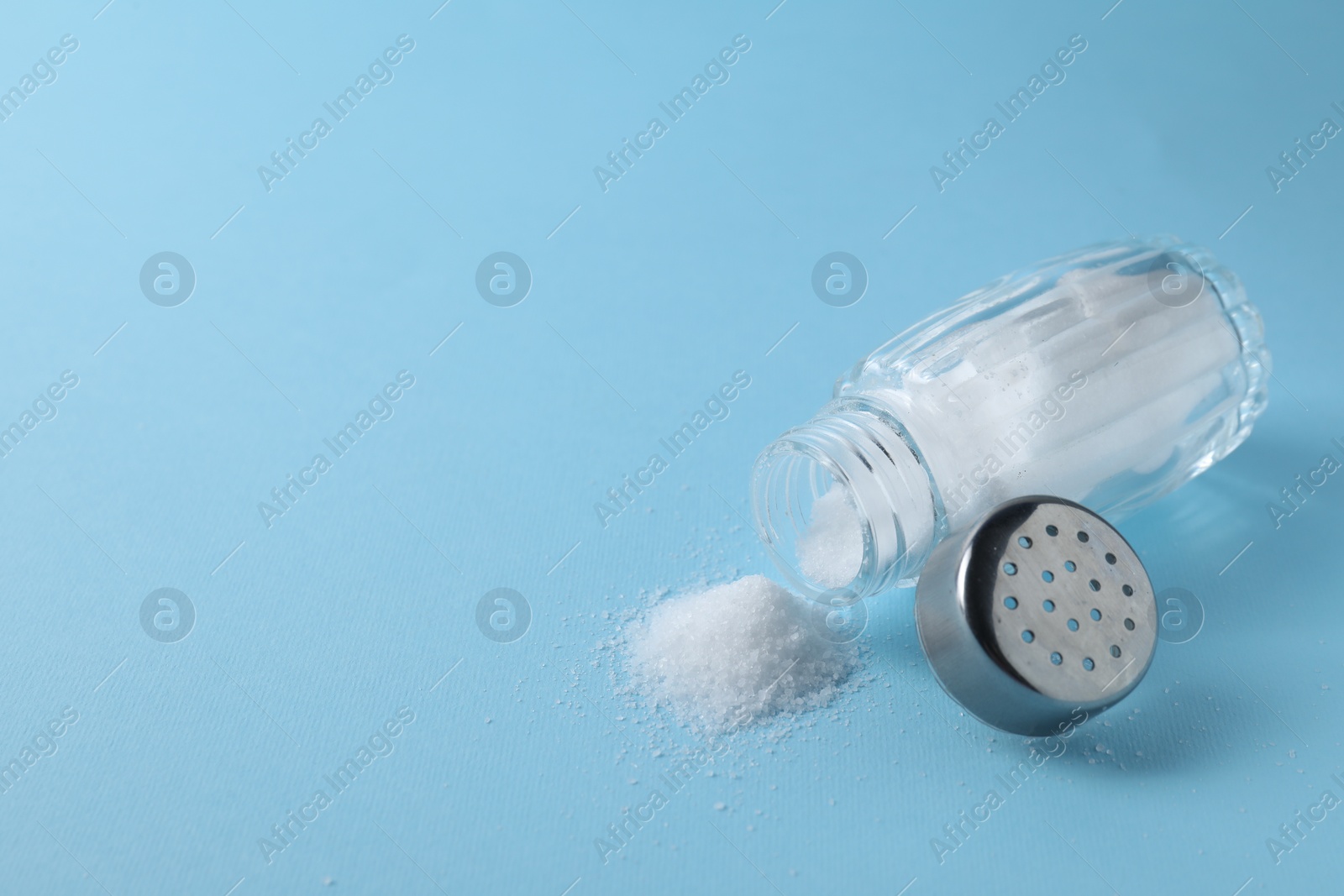 Photo of Organic white salt in shaker on light blue background, closeup. Space for text