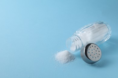 Photo of Organic white salt in shaker on light blue background, closeup. Space for text