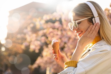 Photo of Young woman with ice cream and headphones listening to music outdoors on sunny day, space for text