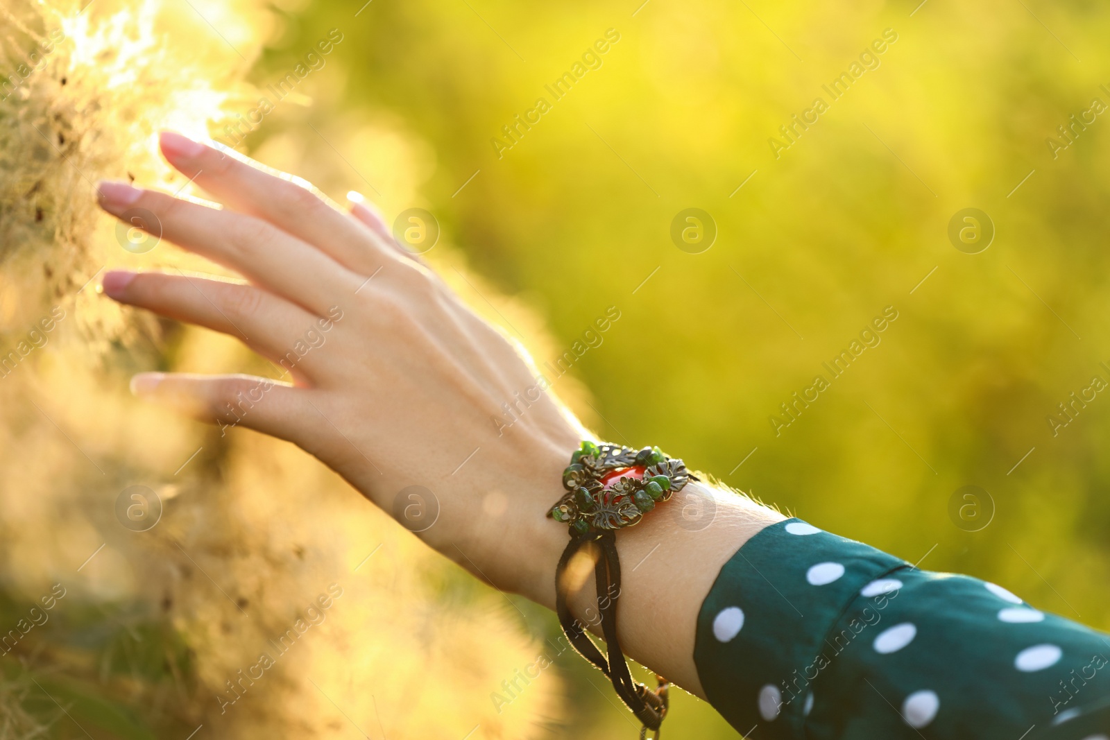 Photo of Young woman wearing beautiful metal bracelet with carnelian and gemstones outdoors, closeup