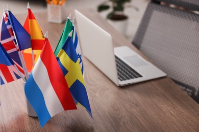 Photo of Different flags and laptop on wooden table indoors, selective focus