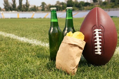 Photo of American football ball with beer and chips on green field grass in stadium. Space for text