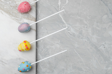 Photo of Egg shaped cake pops and space for text on grey marble table, flat lay. Easter celebration
