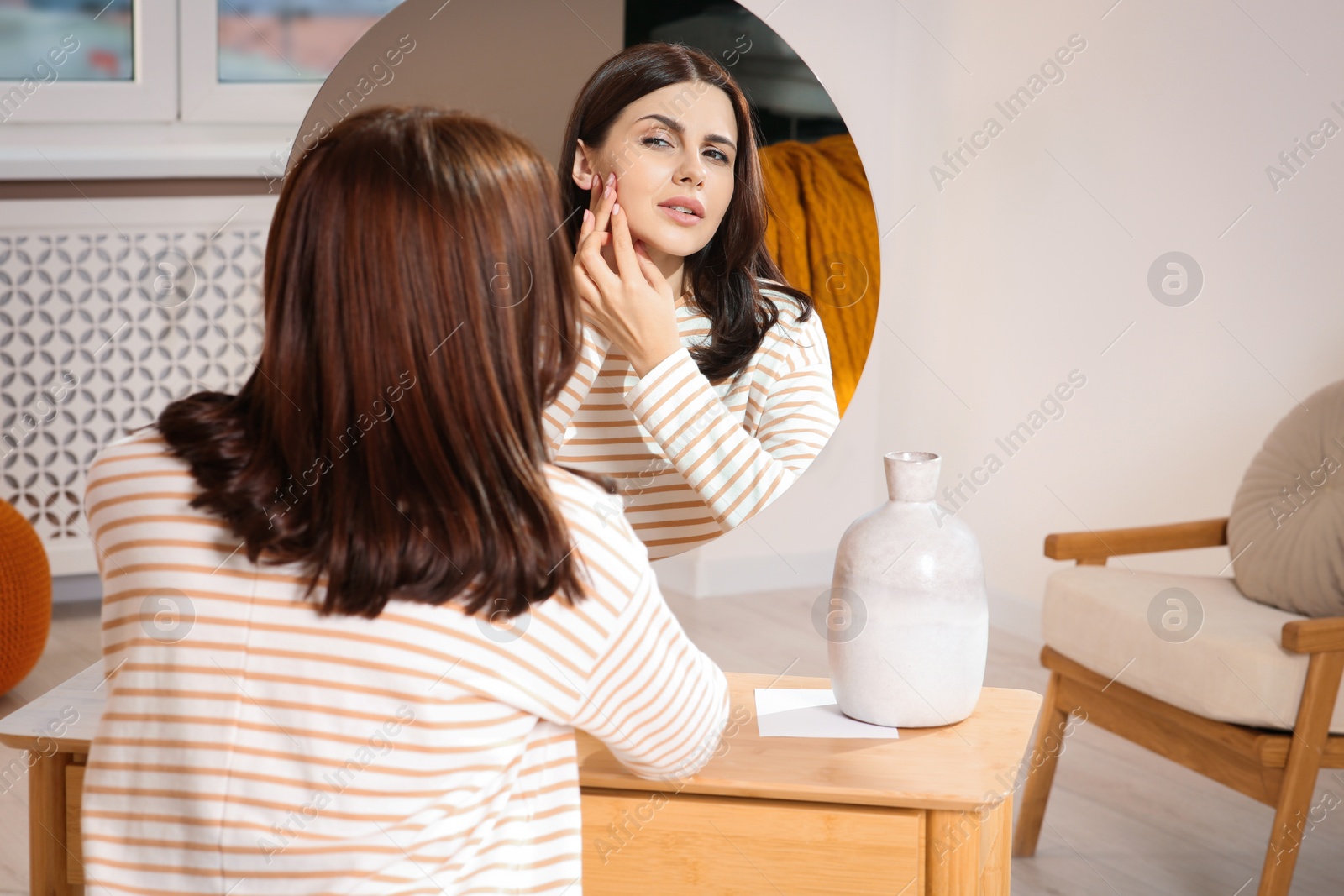 Photo of Young woman looking in mirror and squeezing pimple at home. Hormonal disorders