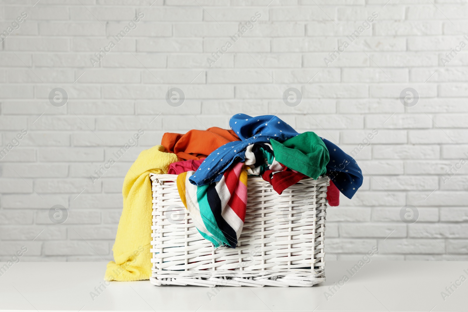 Photo of Wicker basket with laundry on table near white brick wall