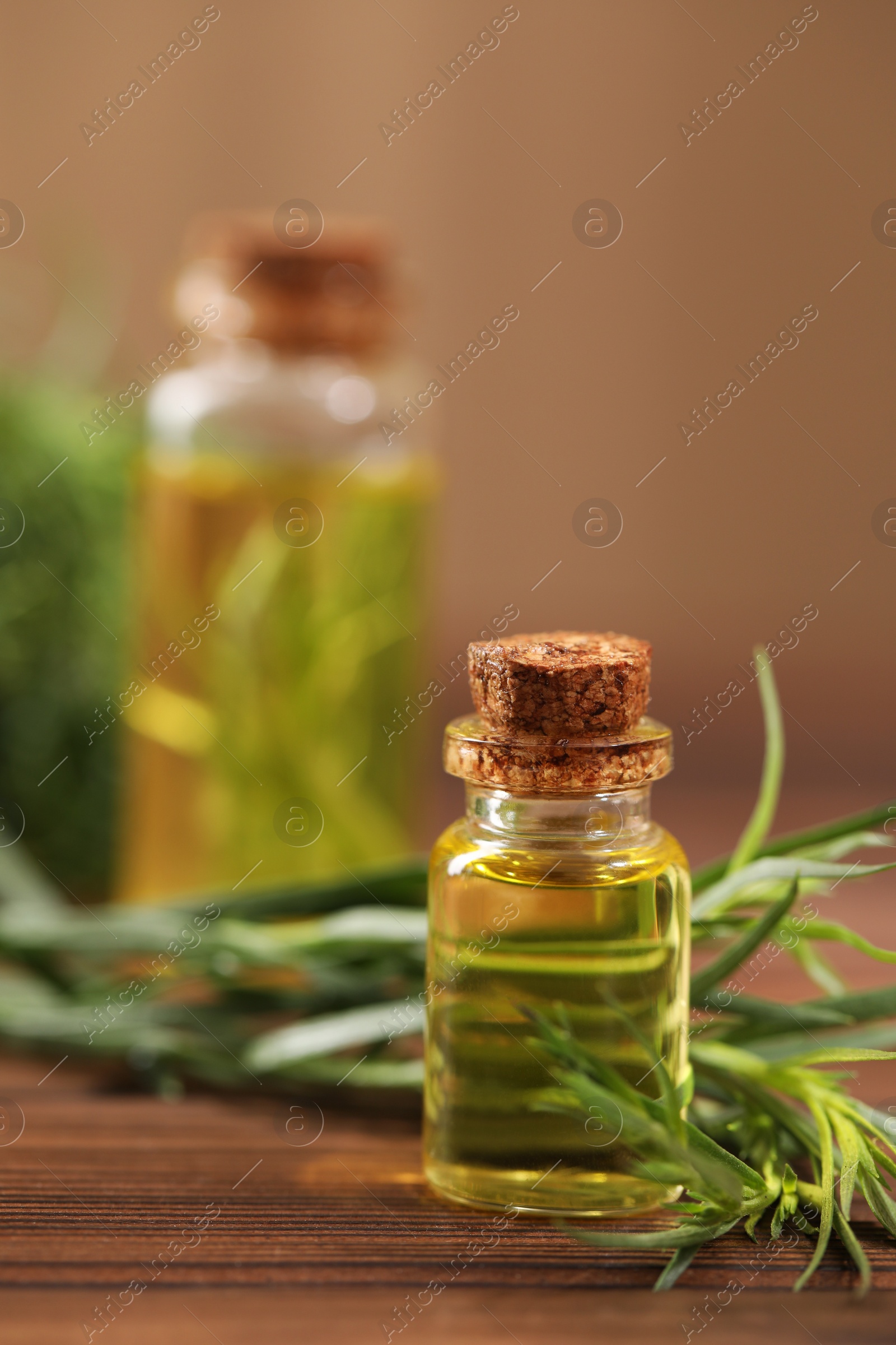 Photo of Bottle of essential oil and fresh tarragon leaves on wooden table