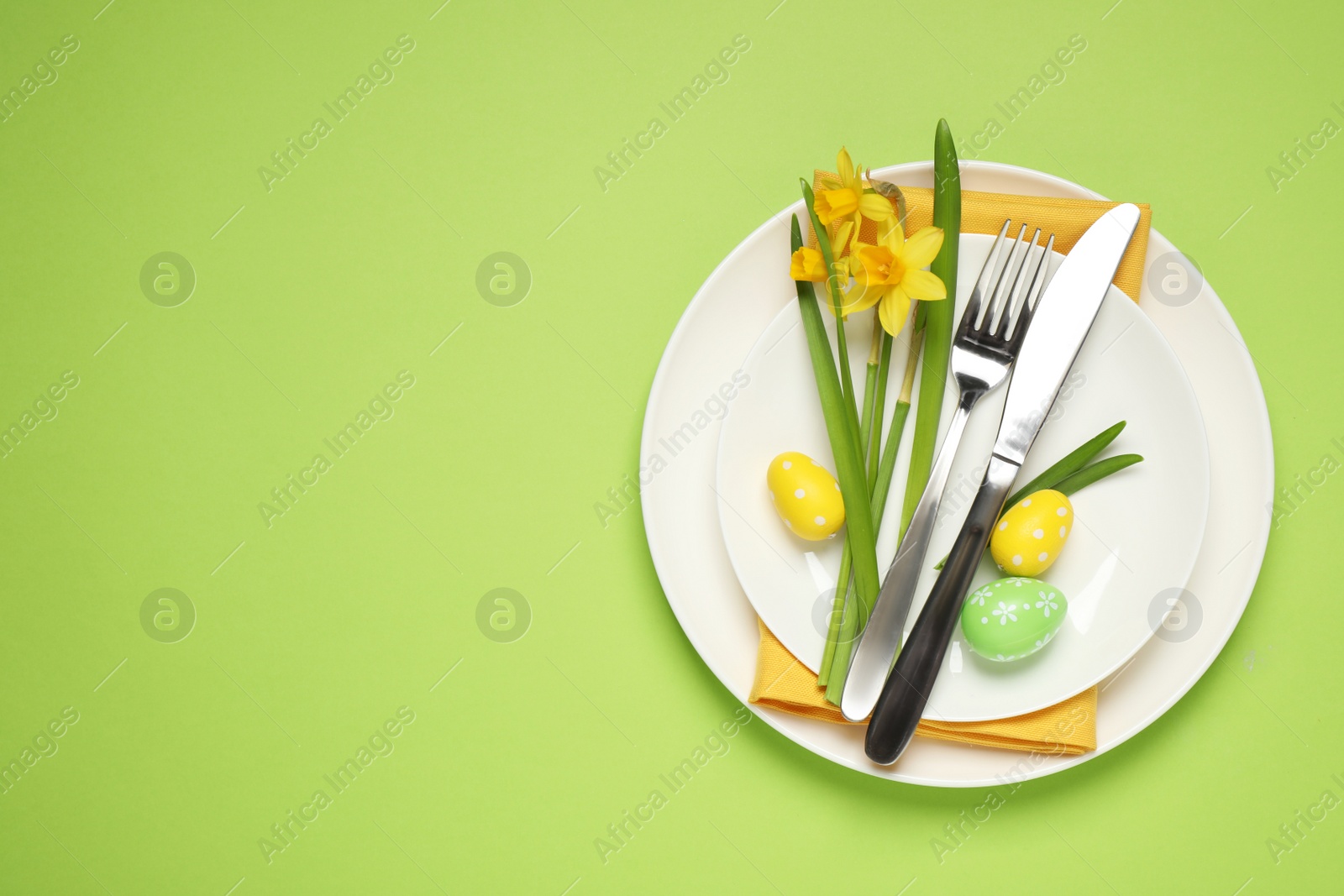 Photo of Festive Easter table setting with beautiful narcissuses and painted eggs, top view. Space for text