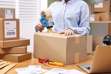 Photo of Parcel packing. Post office worker taping box at wooden table indoors, closeup