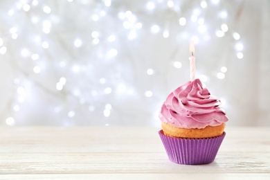 Photo of Delicious birthday cupcake with candle on table against blurred background