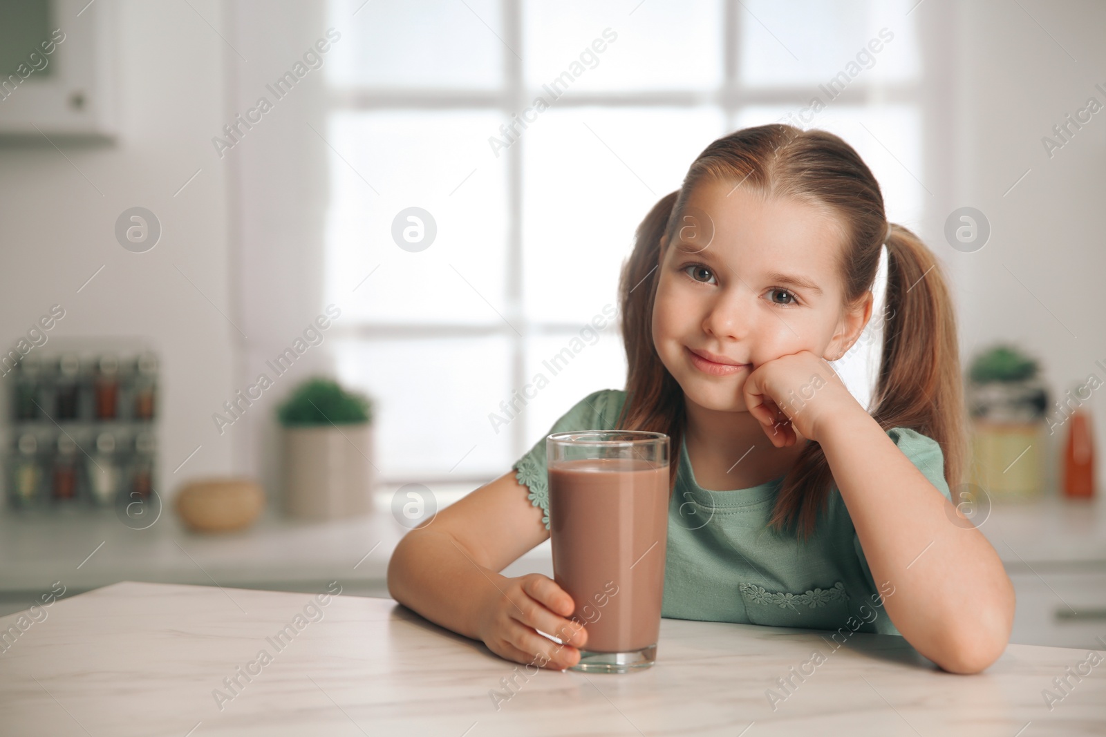 Photo of Cute little child with glass of tasty chocolate milk in kitchen, space for text