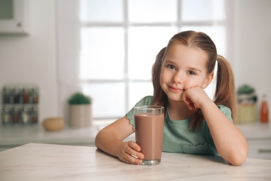 Cute little child with glass of tasty chocolate milk in kitchen, space for text