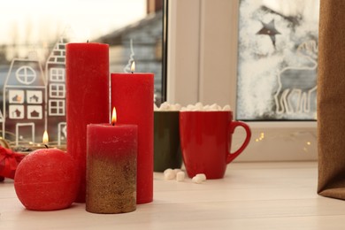 Beautiful burning candles with Christmas decor on white wooden table near window, space for text