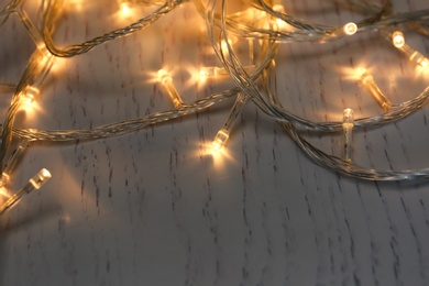 Glowing Christmas lights on white wooden background