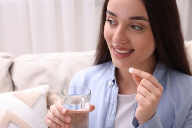 Photo of Beautiful woman with glass of water and pill at home, closeup. Space for text