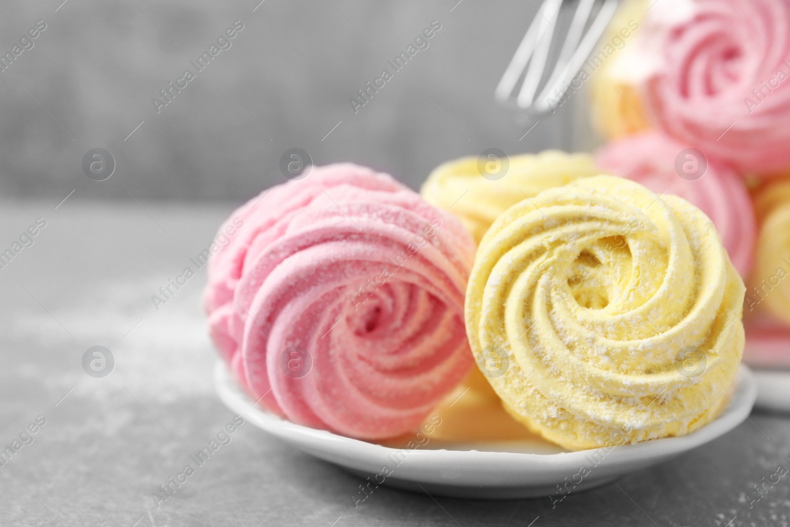 Photo of Delicious pink and yellow marshmallows on grey table, closeup. Space for text