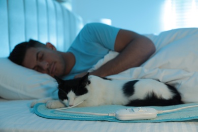 Photo of Man and cat in bed with electric heating pad, focus on cable