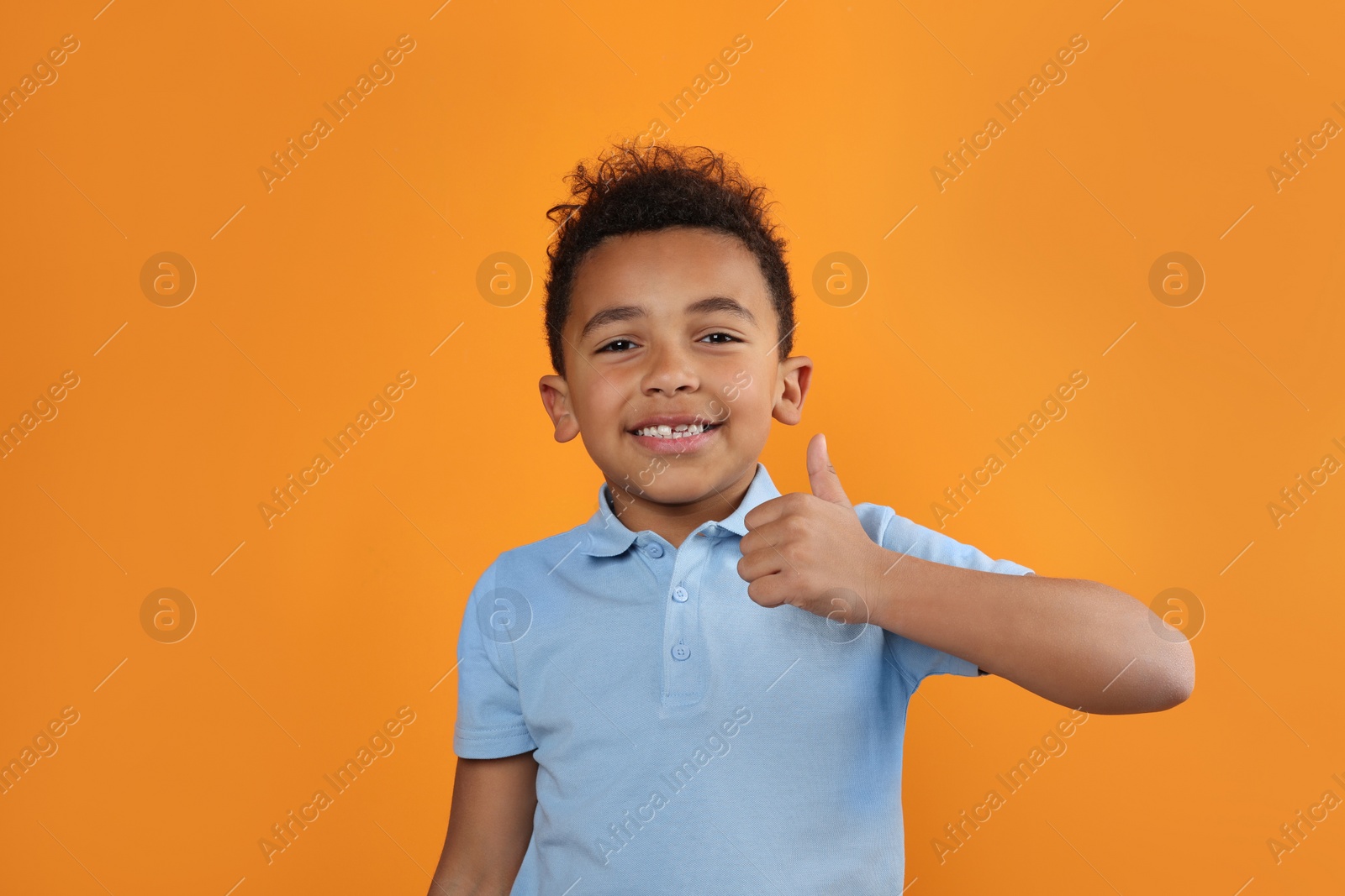 Photo of African-American boy showing thumb up on orange background