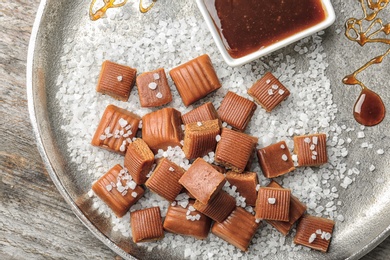 Photo of Delicious caramel candies, sauce and salt on plate, top view