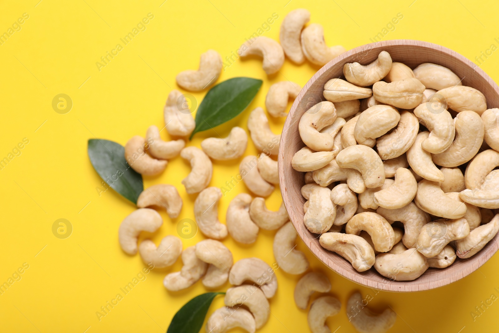 Photo of Tasty cashew nuts and green leaves on yellow background, top view