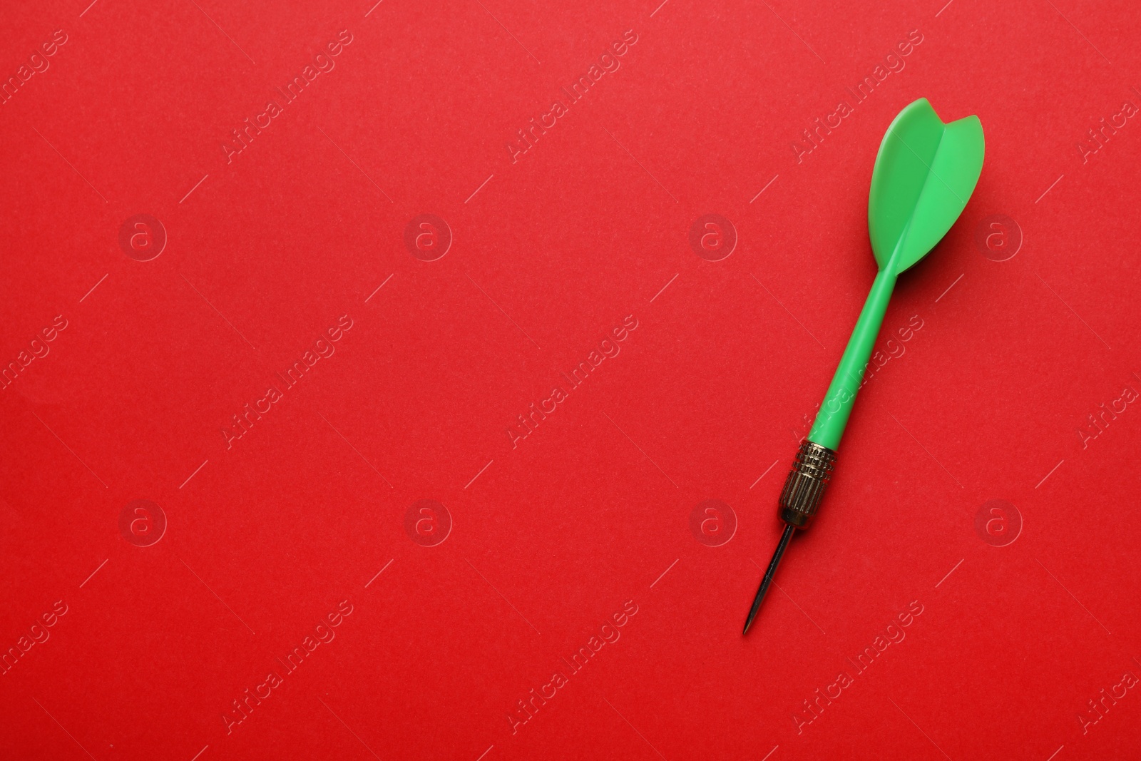 Photo of Green dart arrow on red background, top view with space for text