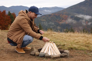 Young man making bonfire in mountains. Camping season