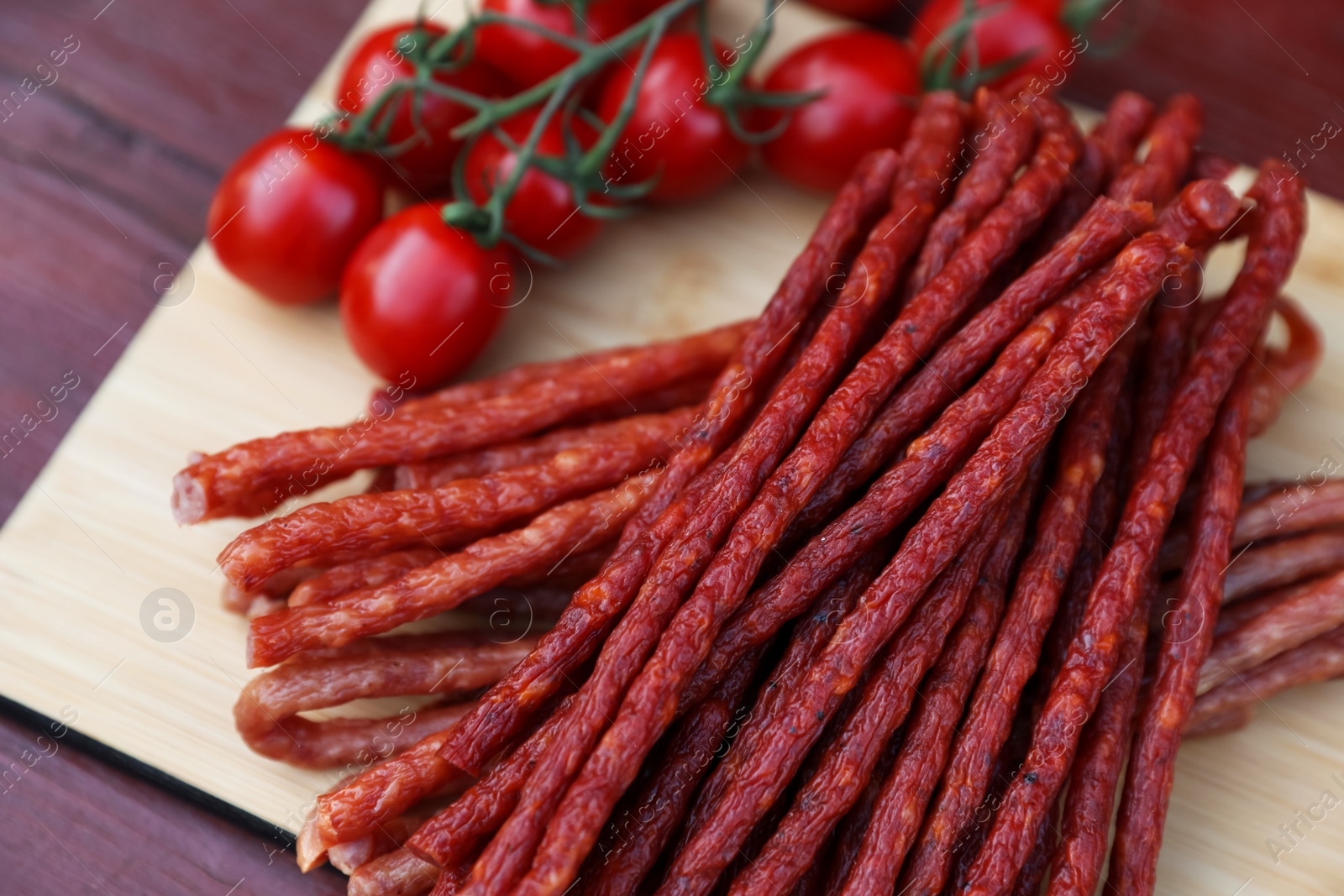 Photo of Tasty dry cured sausages (kabanosy) and tomatoes on wooden table, closeup