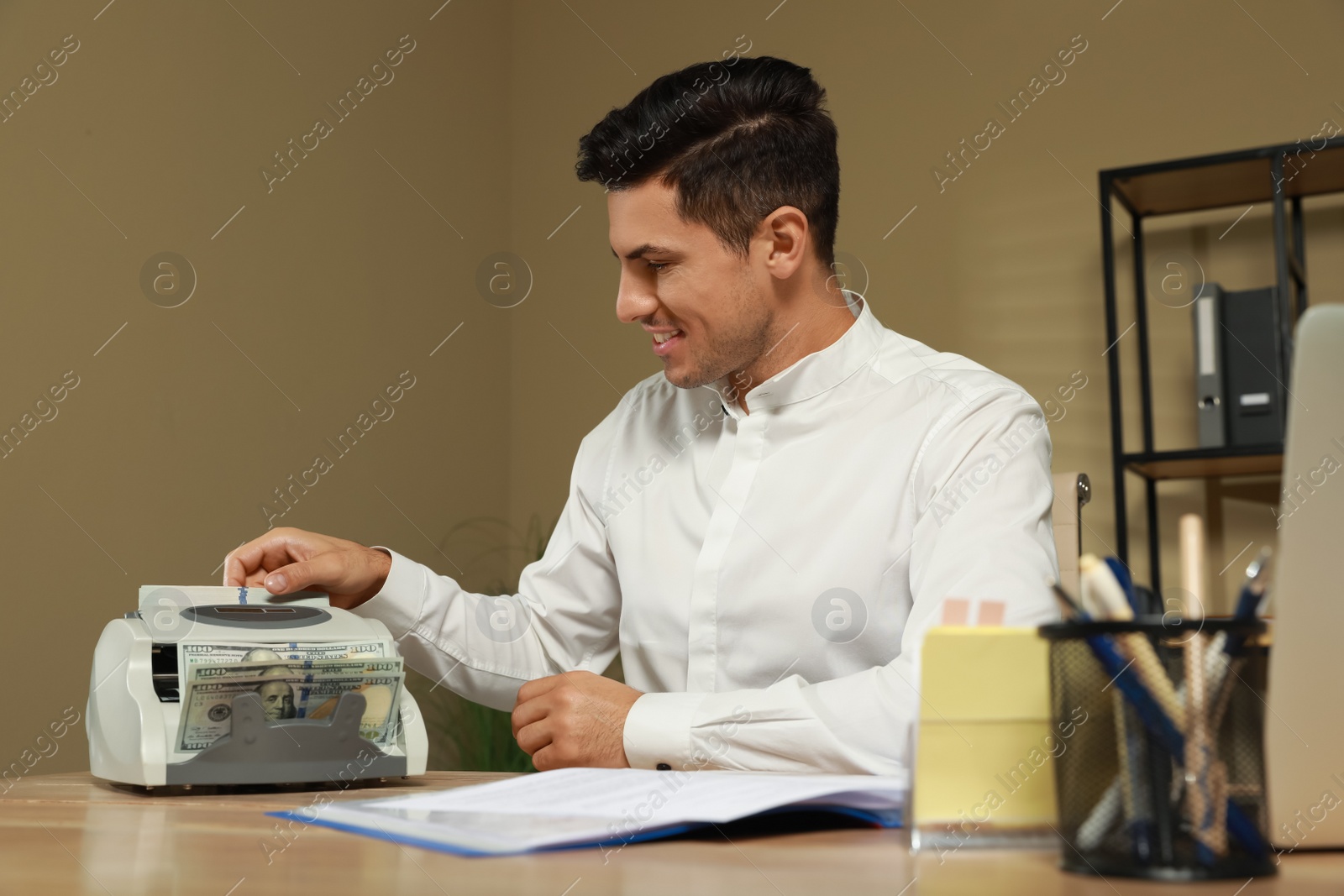 Photo of Man putting money into banknote counter at wooden table indoors