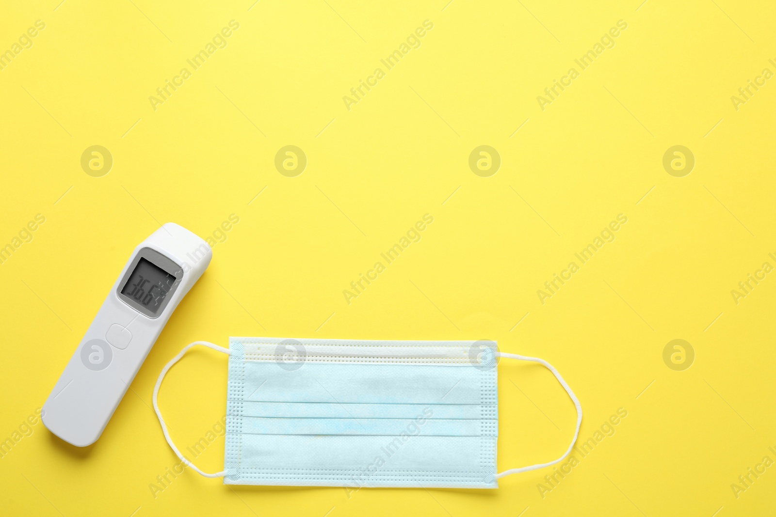 Photo of Infrared thermometer and medical mask on yellow background, flat lay with space for text. Checking temperature during Covid-19 pandemic