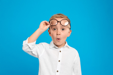 Portrait of cute little boy with glasses on light blue background