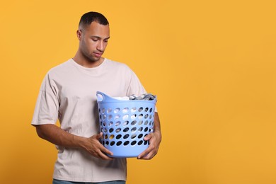 Photo of Young man with basket full of laundry on orange background. Space for text