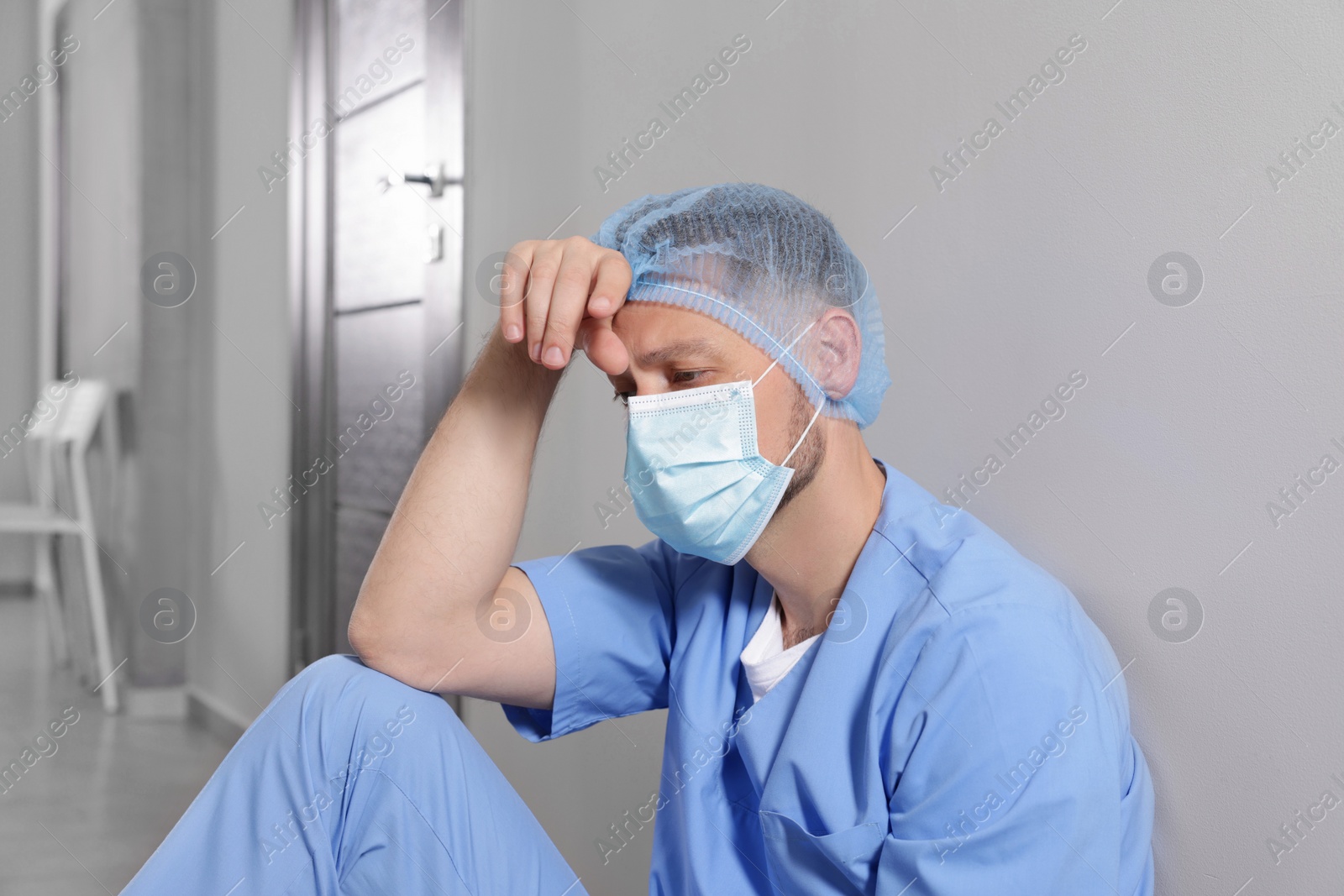 Photo of Exhausted doctor near grey wall in hospital corridor