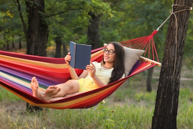 Young woman reading book in comfortable hammock at green garden