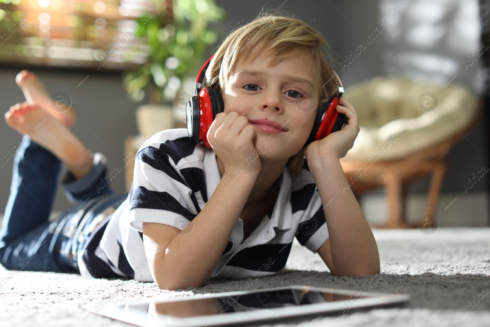 Photo of Cute little boy with headphones and tablet listening to audiobook at home