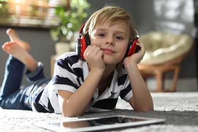 Photo of Cute little boy with headphones and tablet listening to audiobook at home