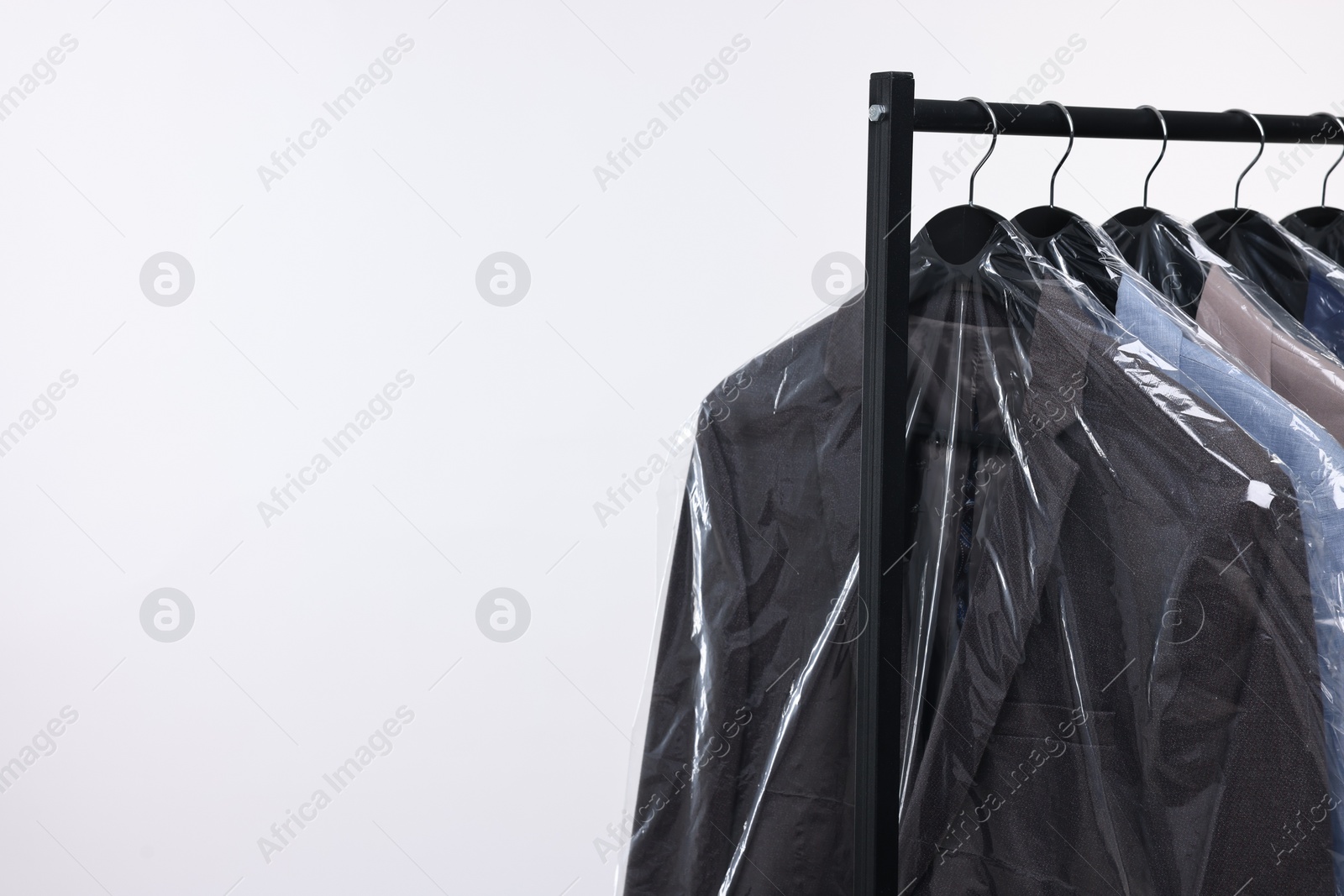 Photo of Dry-cleaning service. Many different clothes in plastic bags hanging on rack against white background, space for text