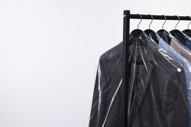 Dry-cleaning service. Many different clothes in plastic bags hanging on rack against white background, space for text