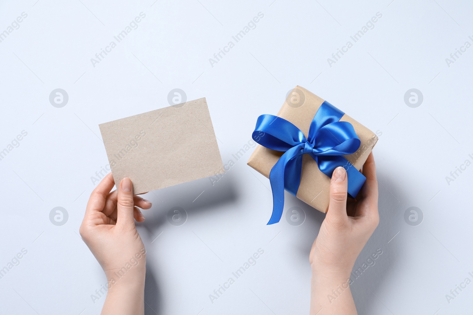 Photo of Woman holding gift box and blank card on white background, top view. Space for text