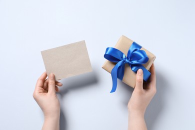 Woman holding gift box and blank card on white background, top view. Space for text