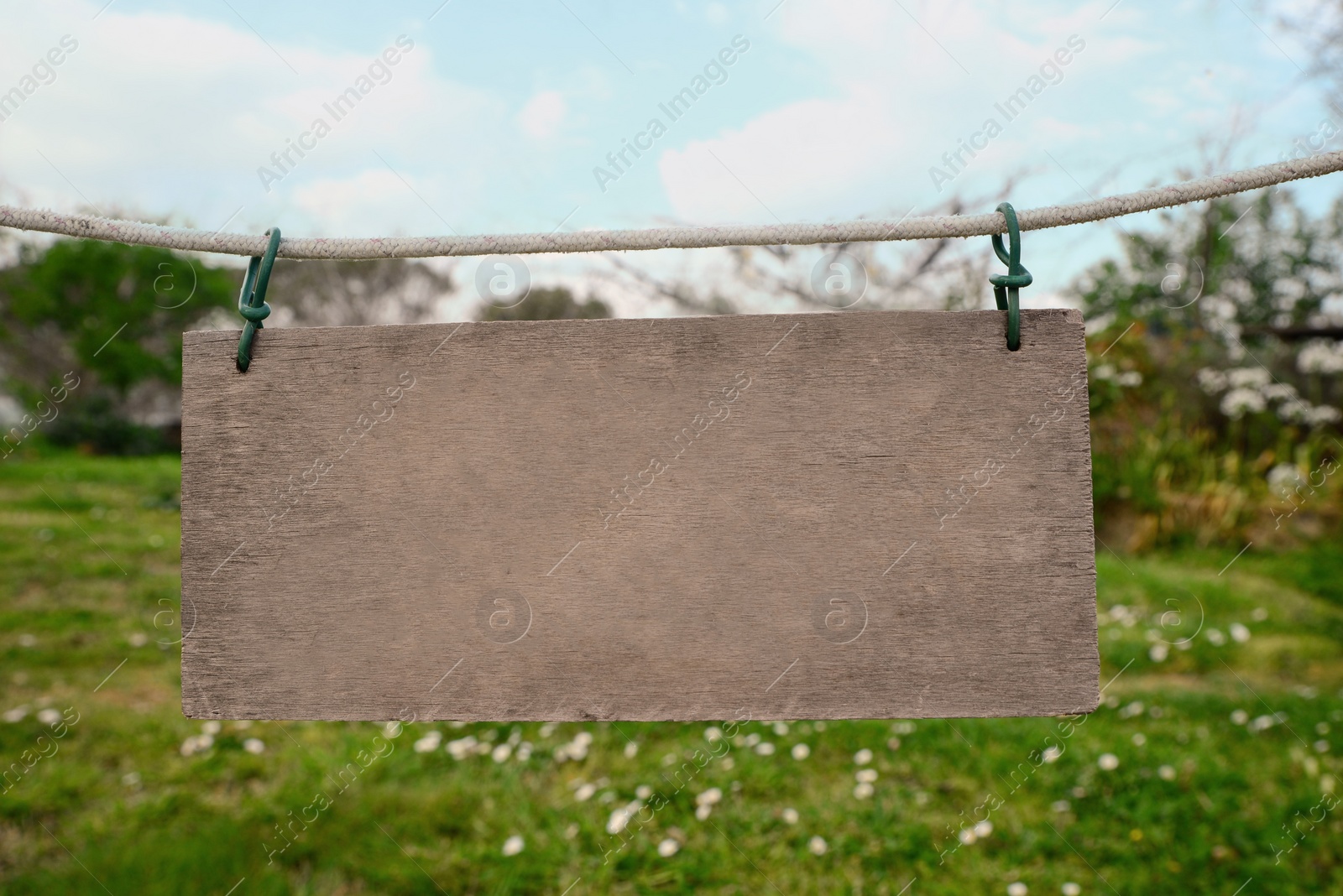 Photo of Blank wooden board hanging on rope in countryside. Space for text