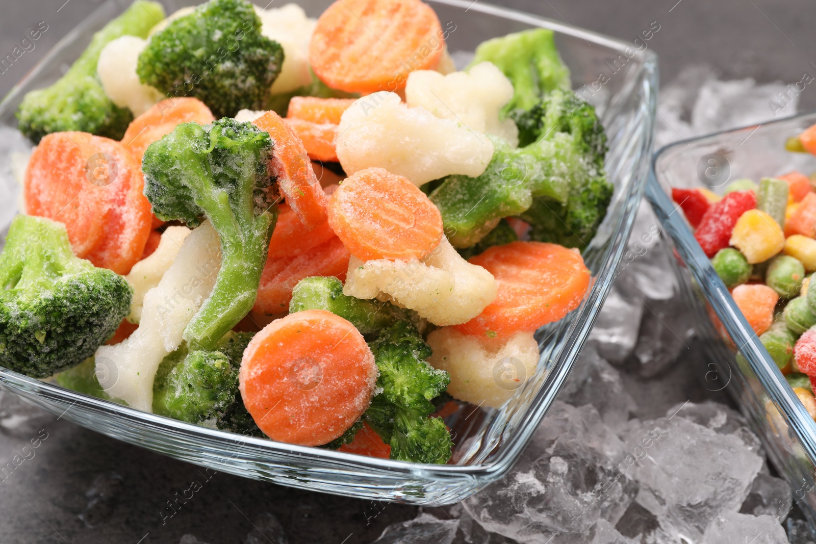 Photo of Mix of different frozen vegetables with ice on grey textured table, closeup