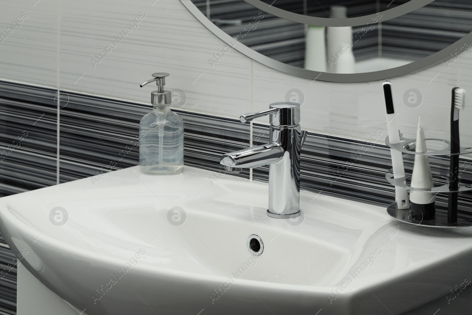 Photo of Clean white sink with shiny water tap and toiletries in bathroom