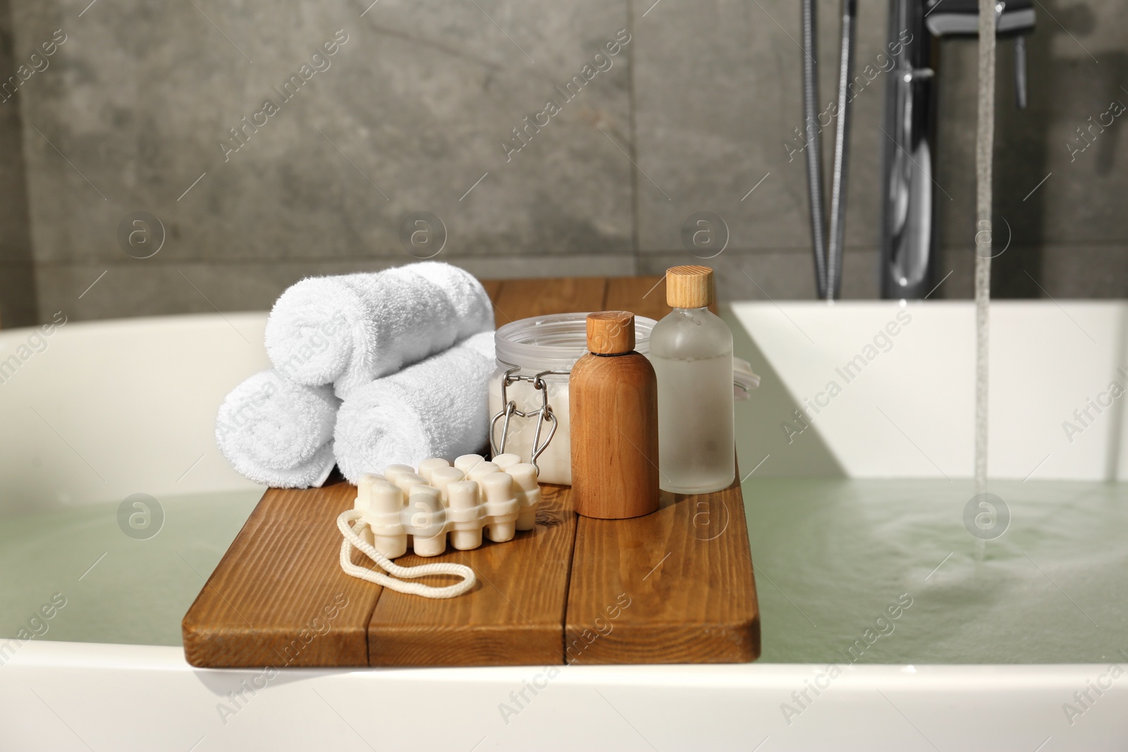 Photo of Wooden tray with spa products and towels on bath tub in bathroom