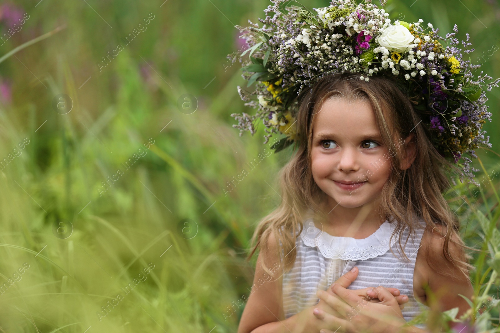 Photo of Cute little girl wearing wreath made of beautiful flowers in field