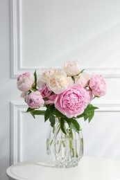 Photo of Bouquet of beautiful peonies in glass vase on white table