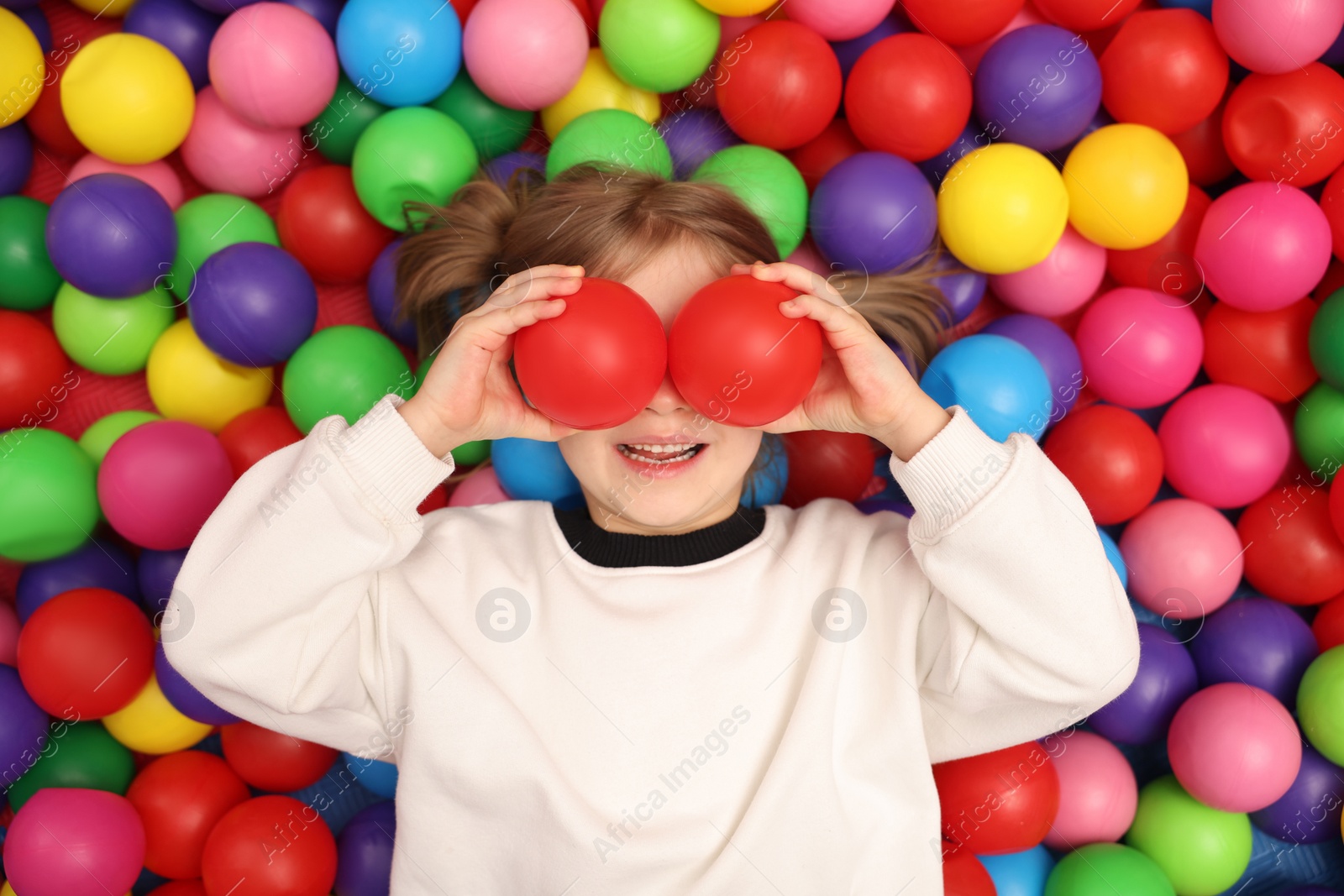 Photo of Happy little girl lying on many colorful balls, top view