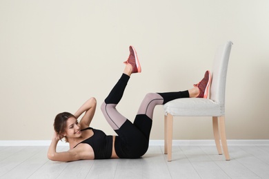 Photo of Young woman exercising with chair near color wall. Home fitness