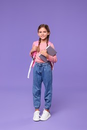 Happy schoolgirl with books on violet background