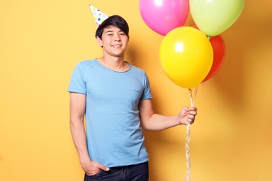 Young man with bright balloons on color background. Birthday celebration