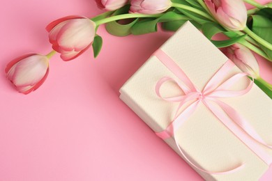 Photo of Beautiful gift box with bow and tulips on pink background, above view. Space for text