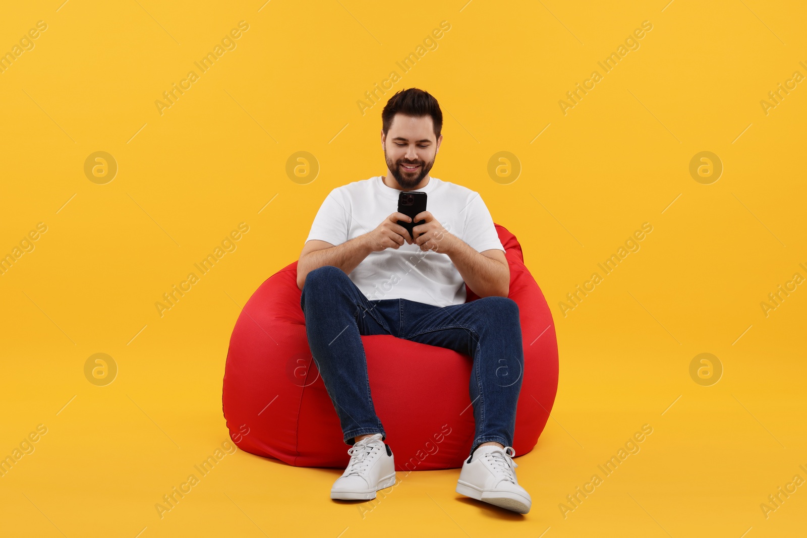 Photo of Happy young man using smartphone on bean bag chair against yellow background